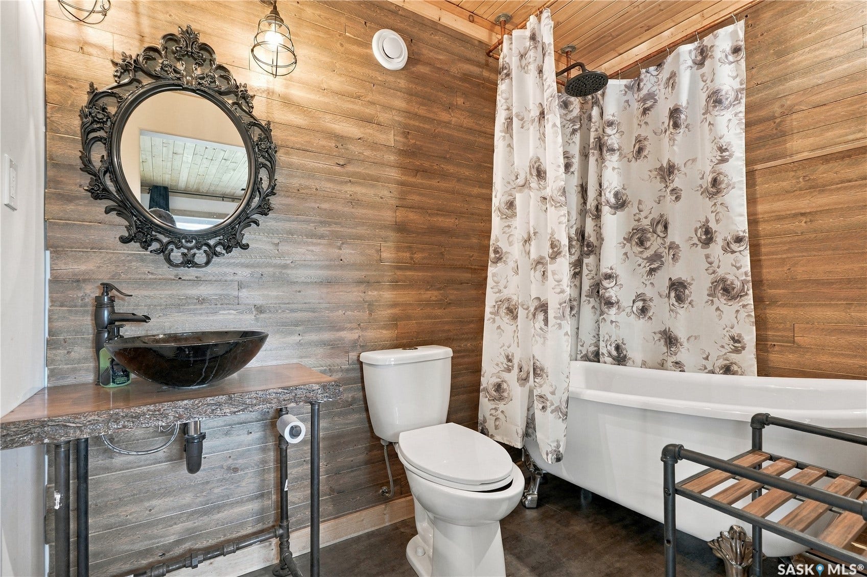 Wood-paneled bathroom featuring a vessel sink with a dark faucet, ornate mirror, and a freestanding clawfoot bathtub with a shower attachment