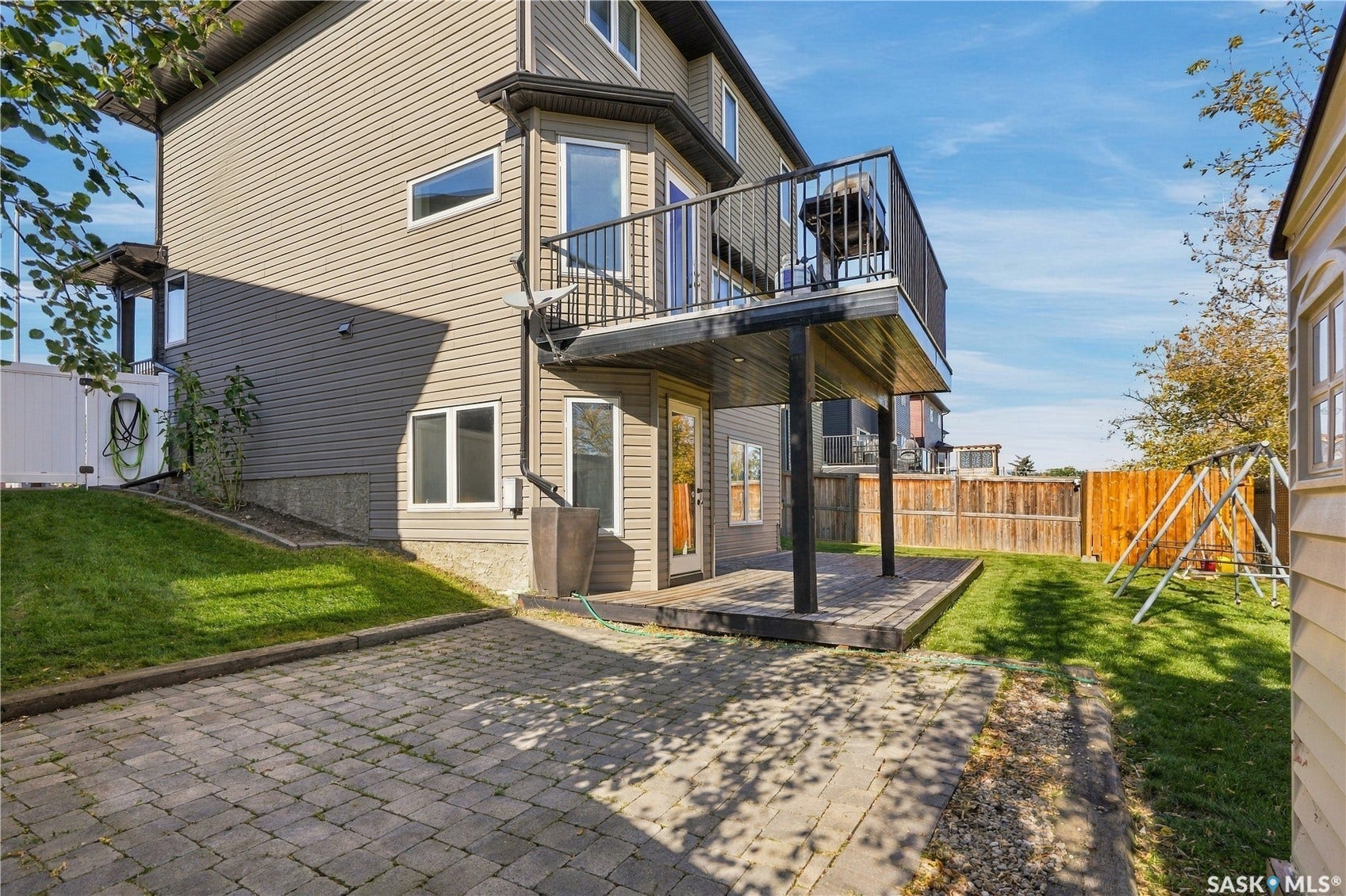 Lower-level patio with an upper-level balcony, paved stone patio, and a manicured lawn
