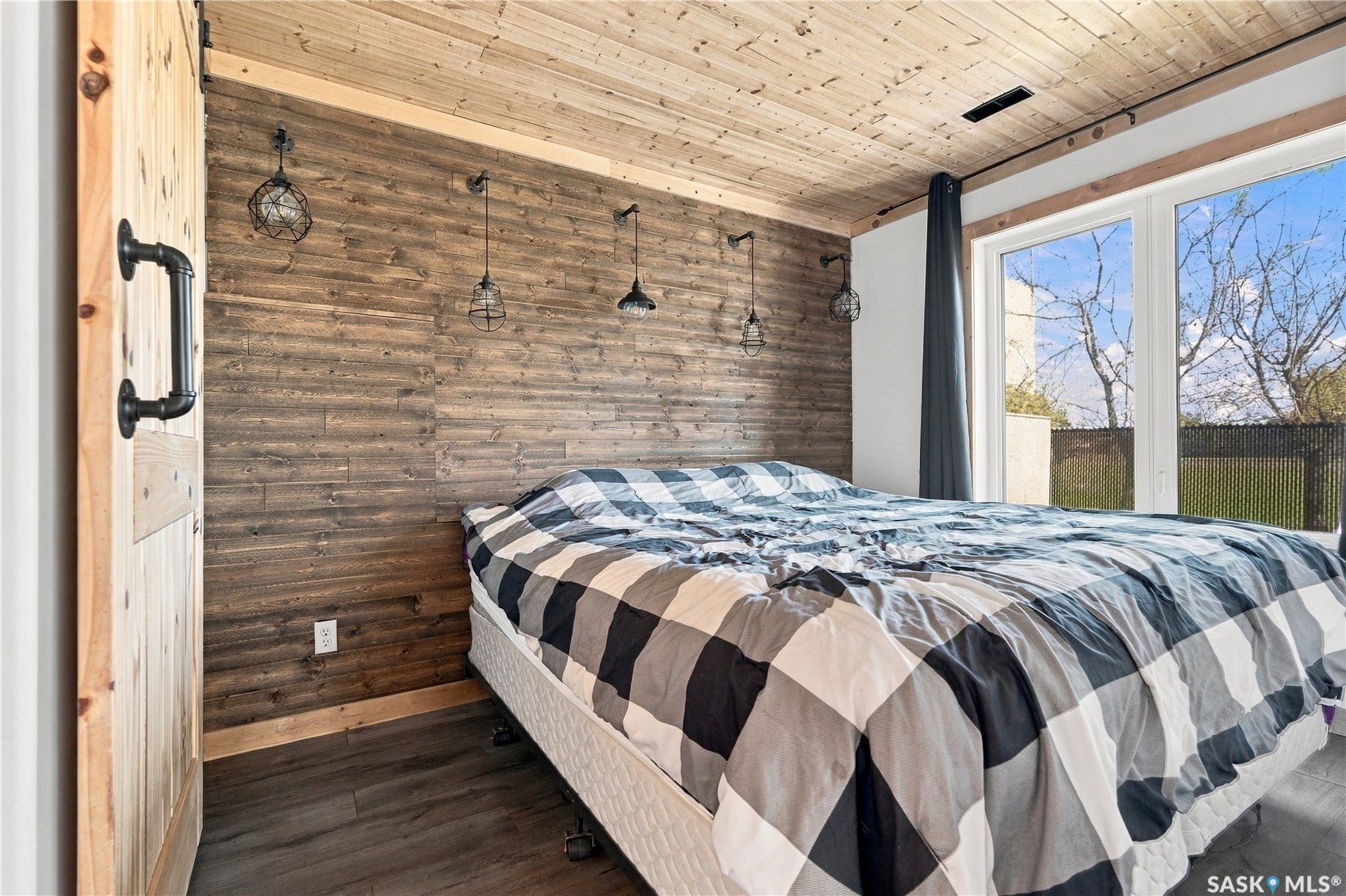 Wood-paneled ceiling, accent wall with industrial-style sconces, large window, and laminate flooring