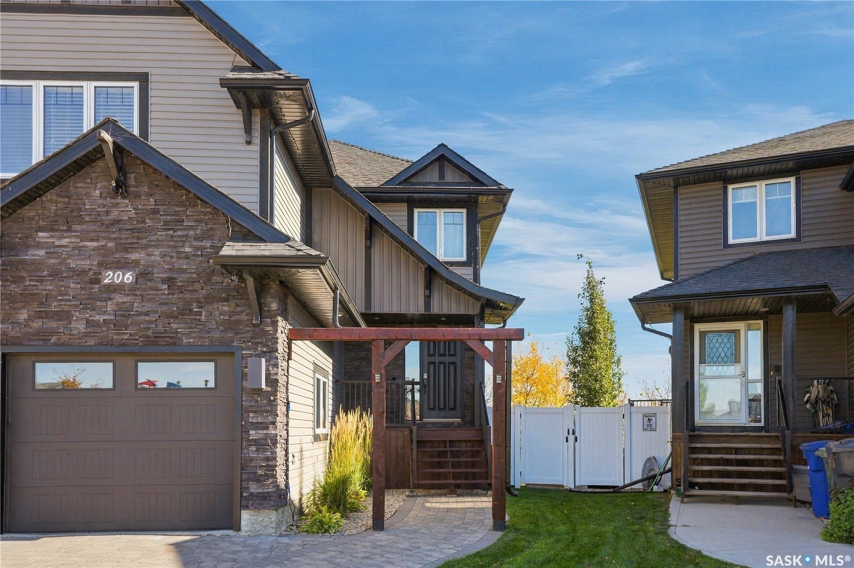 Stacked stone facade, attached garage, wood pergola, paved walkway, and private fenced yard