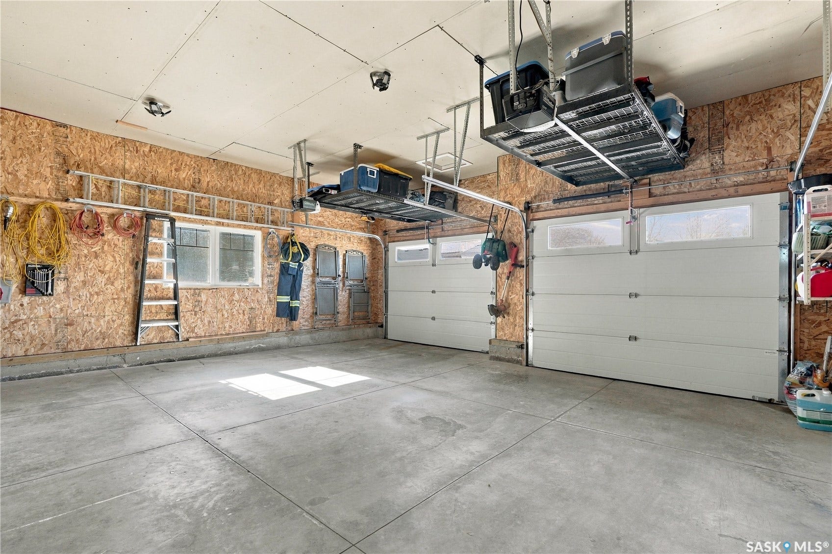 Garage with two overhead doors, concrete flooring, exposed wood-panel walls, and ceiling-mounted storage racks