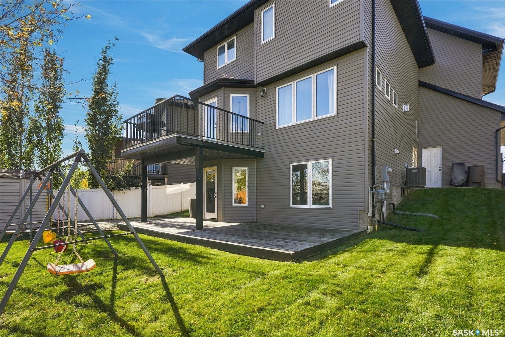 Multi-level exterior featuring a second-story balcony with dark railings, a ground-level patio, and a sloped lawn