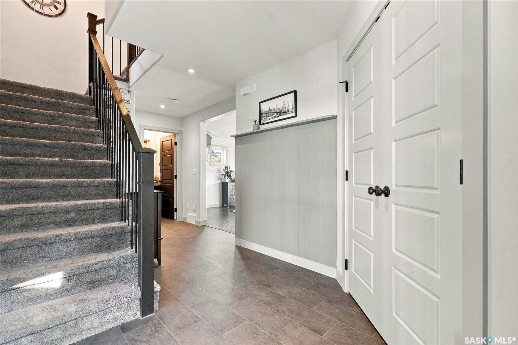 Staircase with carpeted treads and wood balusters, linoleum flooring, paneled interior doors with black hardware, and vertical panel accent wall
