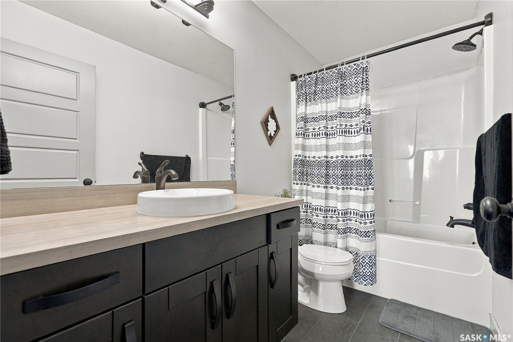 Bathroom featuring a dark wood-finish vanity with a vessel sink, a full-width mirror, a white bathtub with shower, and dark flooring