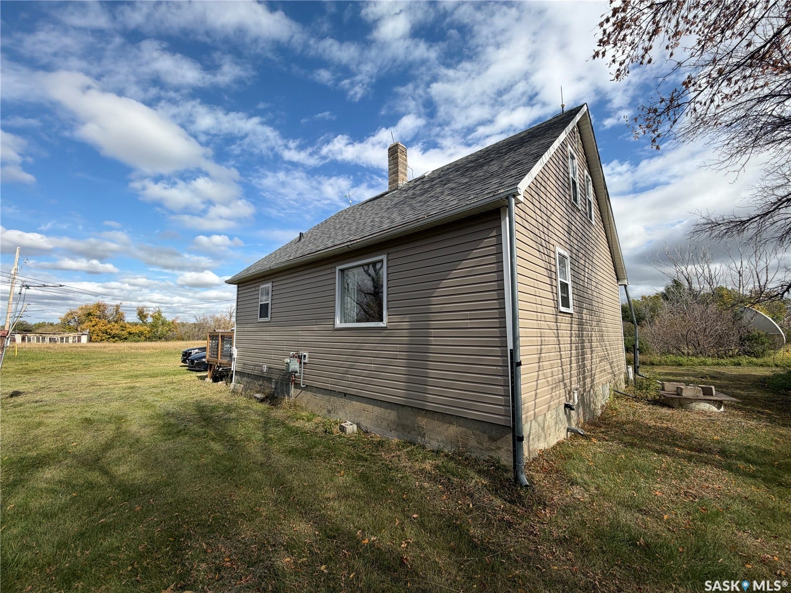 Beige siding exterior with a dark shingle roof, white trim windows, and a masonry chimney