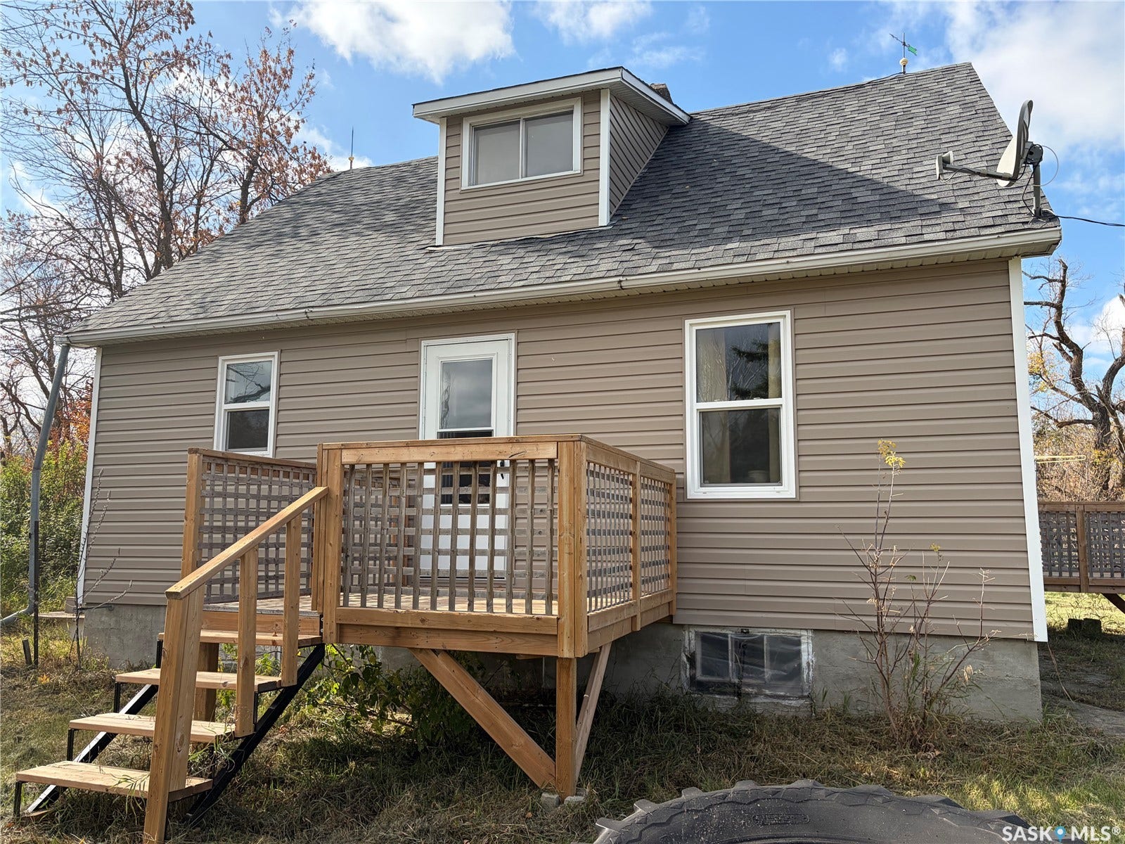 Rear exterior featuring light brown siding, a dormer window, a dark shingle roof, and a wood deck with stairs