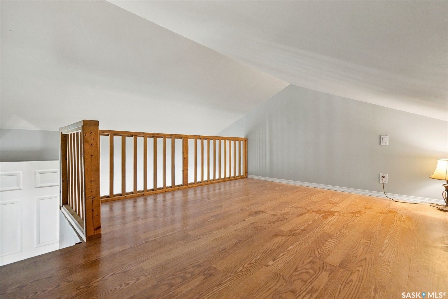 Expansive loft space with wood-finish flooring, natural wood railing, and light-toned walls