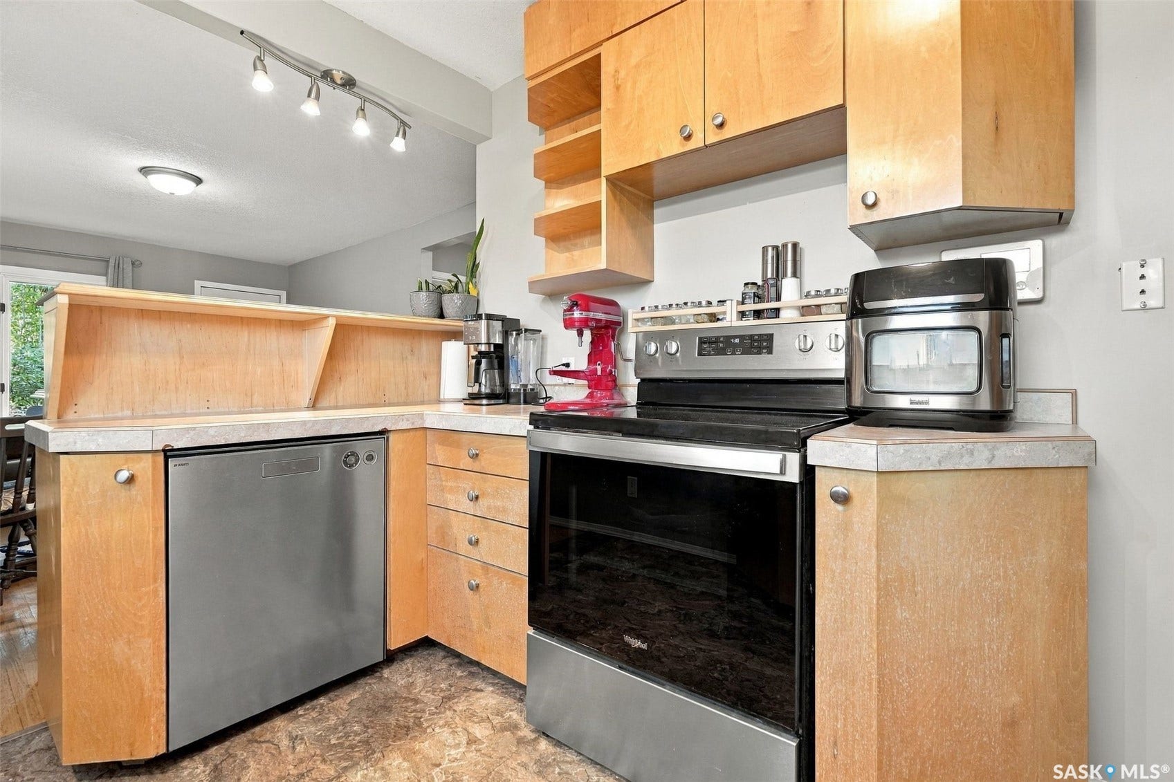 Wood cabinetry with silver hardware, stainless steel dishwasher, stainless steel range, light-toned countertop, and track lighting