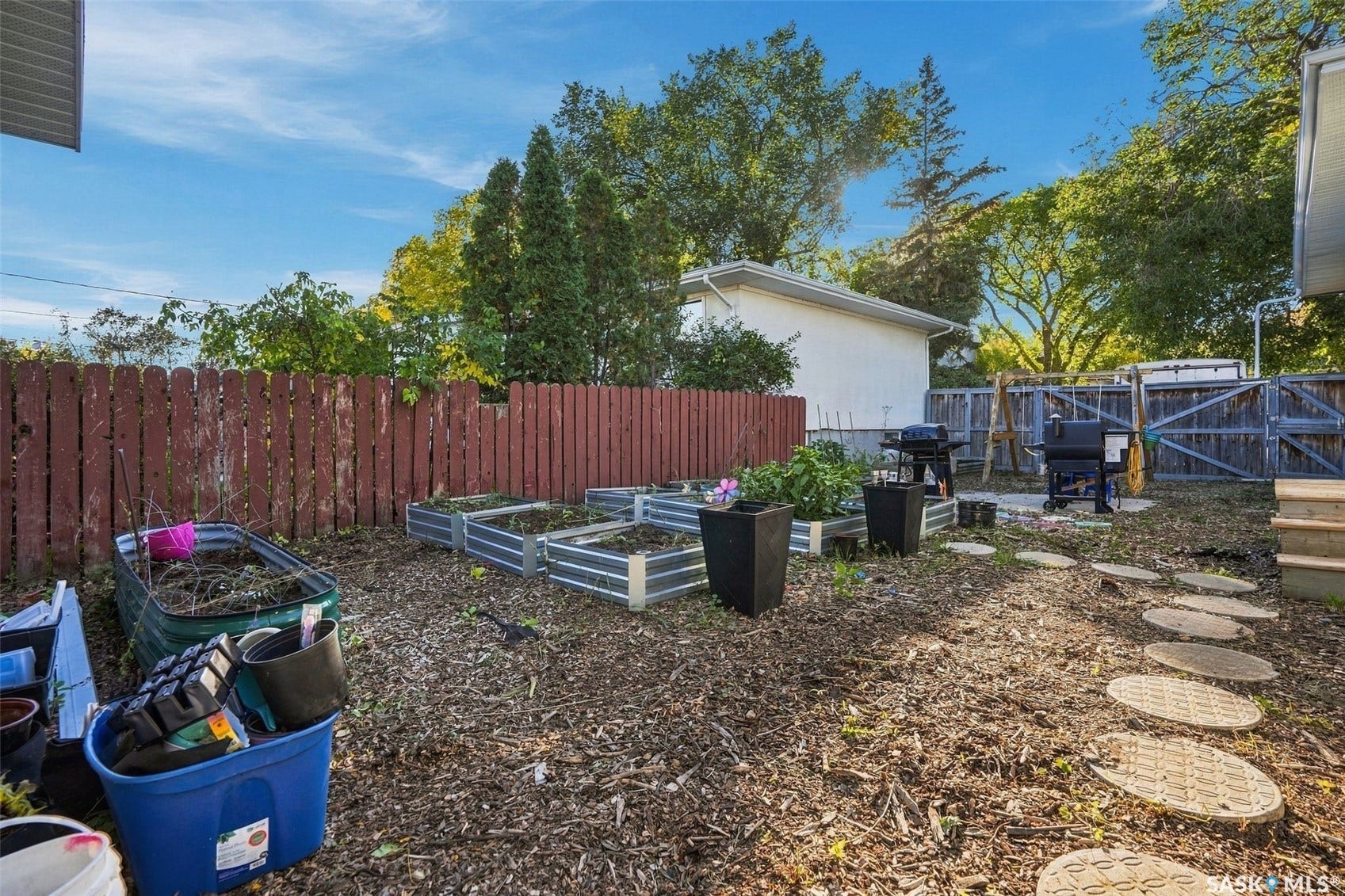 Expansive backyard featuring a red wooden fence, raised garden beds, and a stepping stone pathway