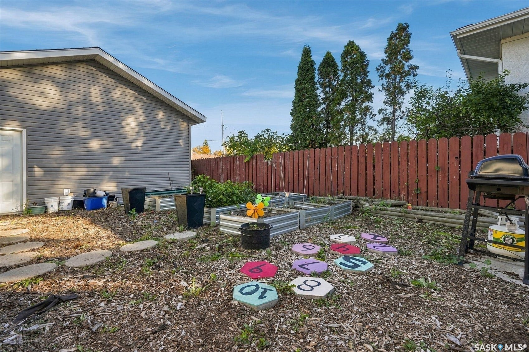 Expansive backyard featuring a red wood fence, multiple raised garden beds, and stepping stones