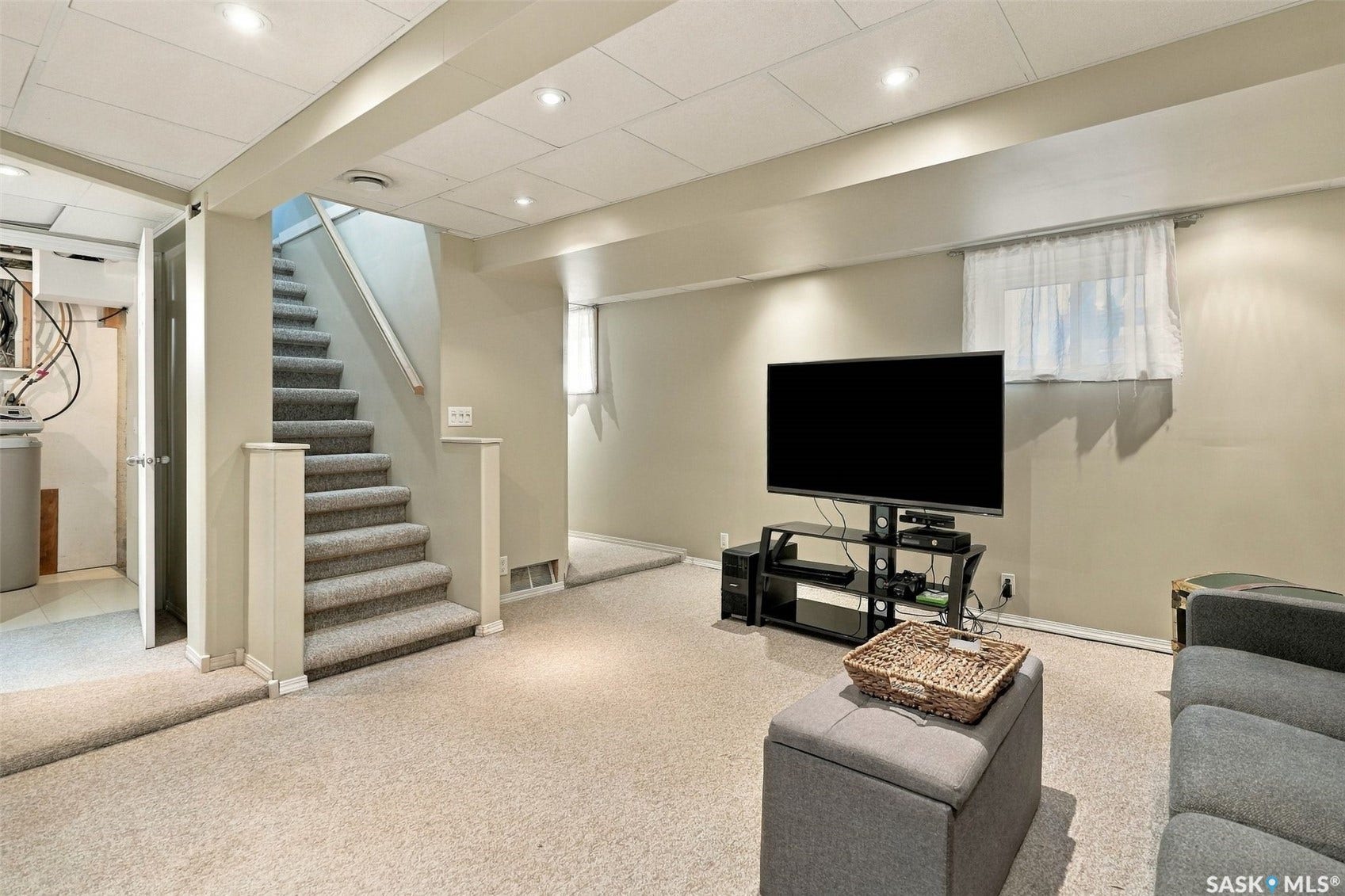 Finished basement recreation room featuring neutral carpeting, recessed ceiling lighting, and a built-in media console with shelving