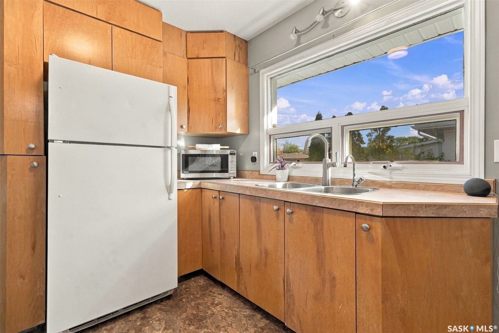 Wood cabinetry and countertops, with a double basin stainless steel sink, large window, and integrated refrigerator