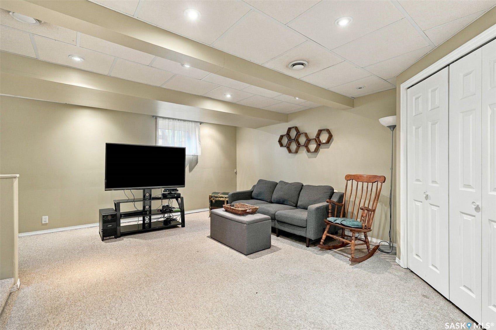 Carpeted room featuring a drop ceiling with recessed lighting, exposed ceiling beams, and a window with white blinds