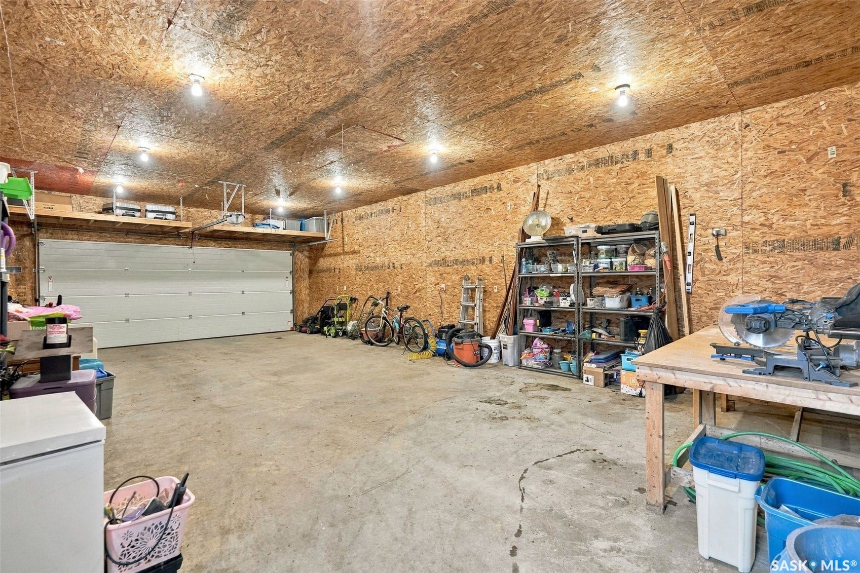 Spacious garage with exposed wood-finish walls and ceiling, concrete flooring, and multiple overhead light fixtures