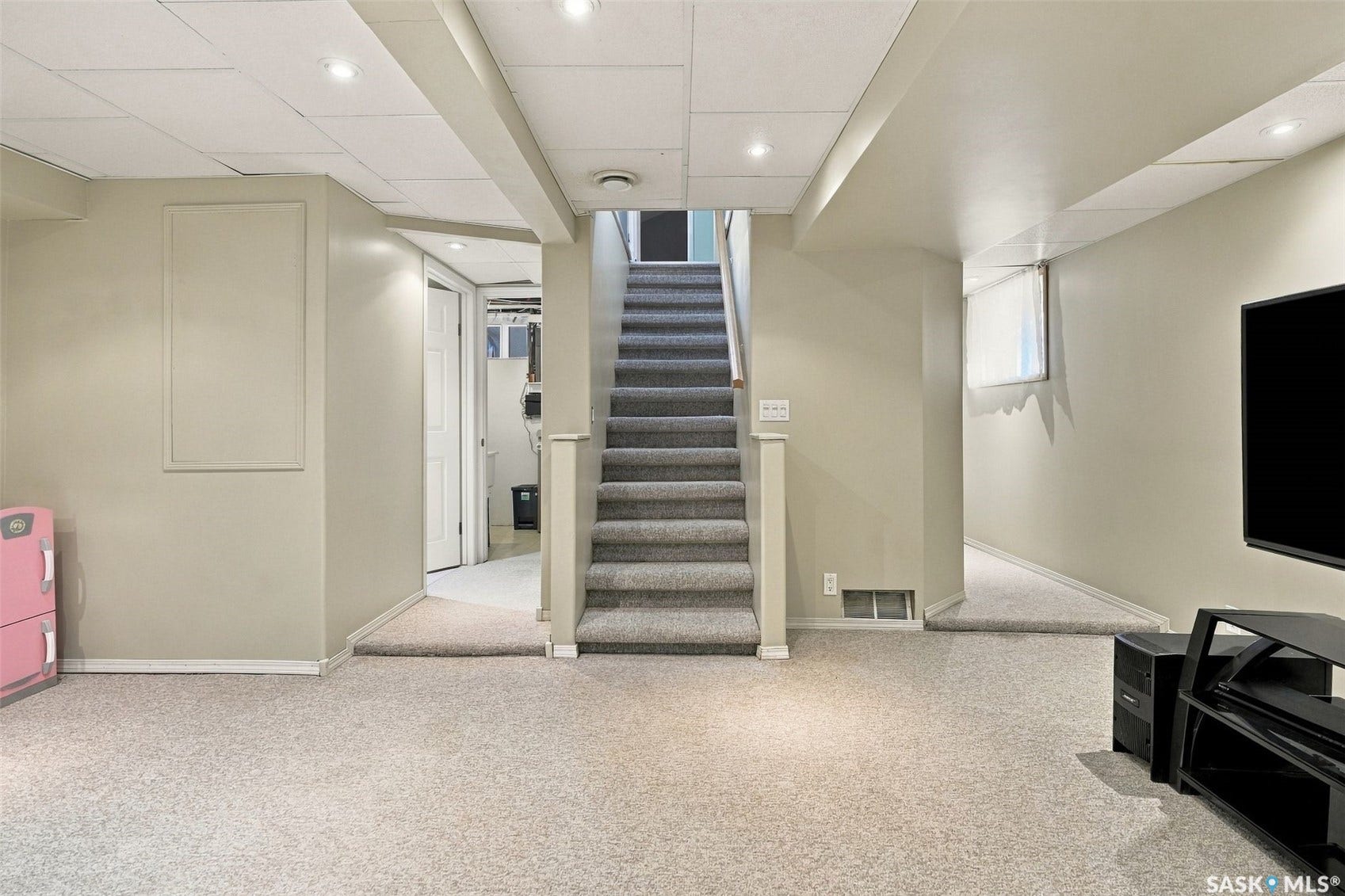Carpeted flooring throughout, dropped ceiling with recessed lighting, painted walls, and carpeted staircase with wood railing