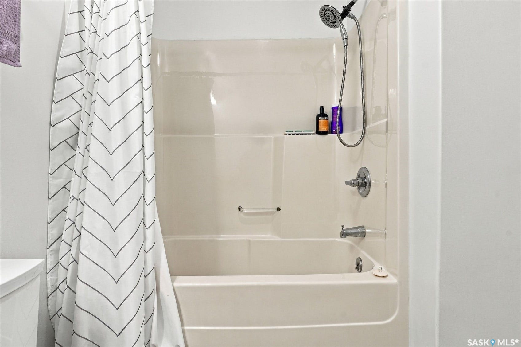 Bathtub and shower combination with chrome fixtures and built-in shelving
