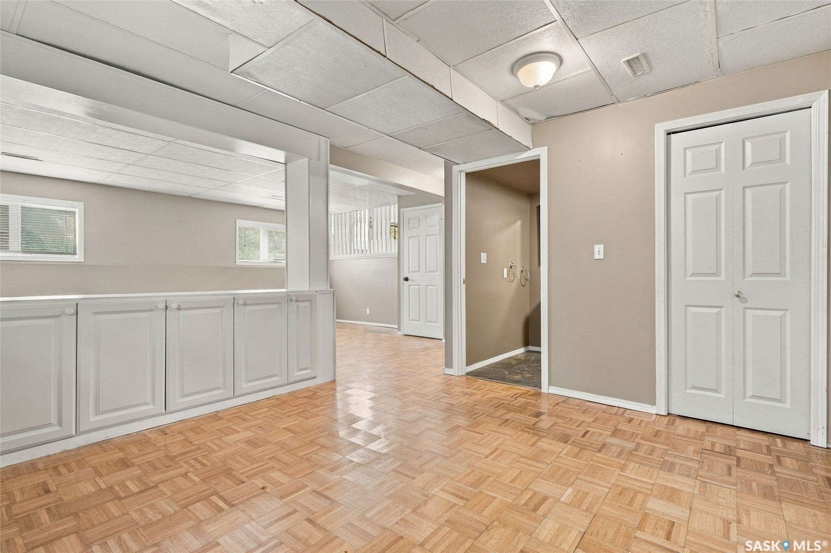 Wood-finish parquet flooring, built-in white cabinetry, two paneled doors, recessed ceiling lighting, and two windows