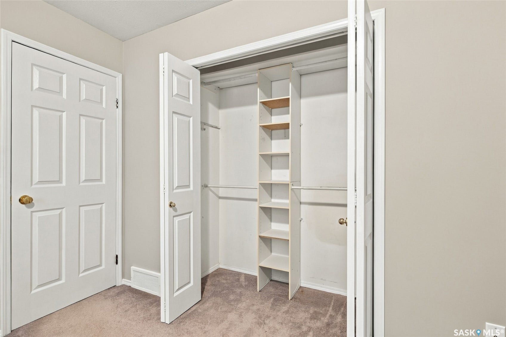 Wardrobe featuring built-in shelving and hanging rods, neutral-toned carpeting, and a white six-panel door