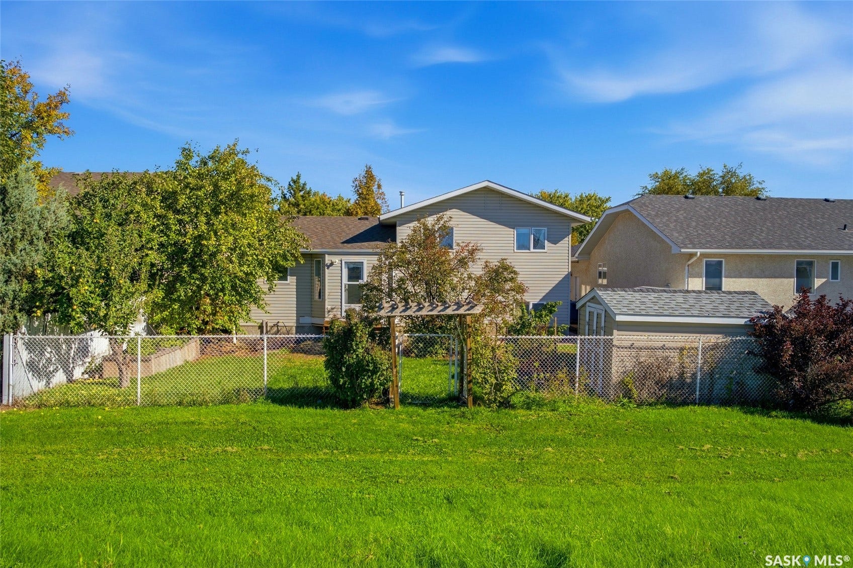 Expansive rear lawn with established perimeter fencing, featuring a garden arbor and storage shed