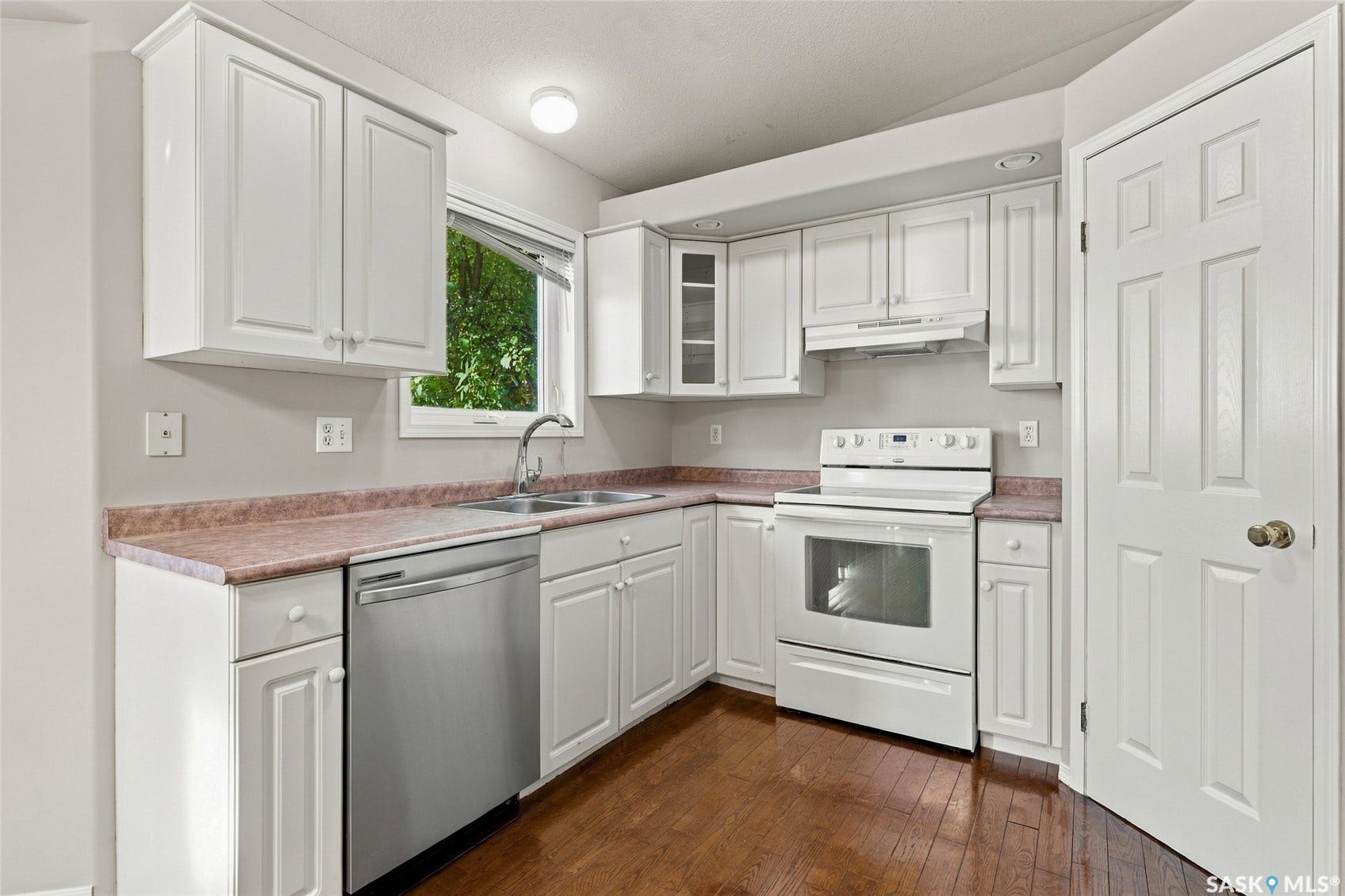 Kitchen featuring white cabinetry, a stainless steel dishwasher, white range with overhead microwave, a double basin sink, and wood-finish flooring