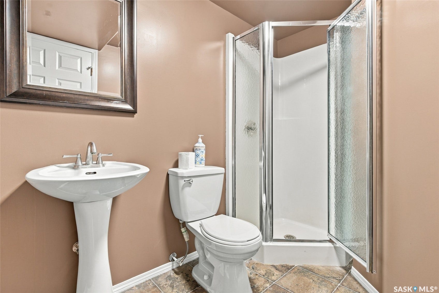 Pedestal sink with chrome faucet, toilet, and shower enclosure with textured glass panels