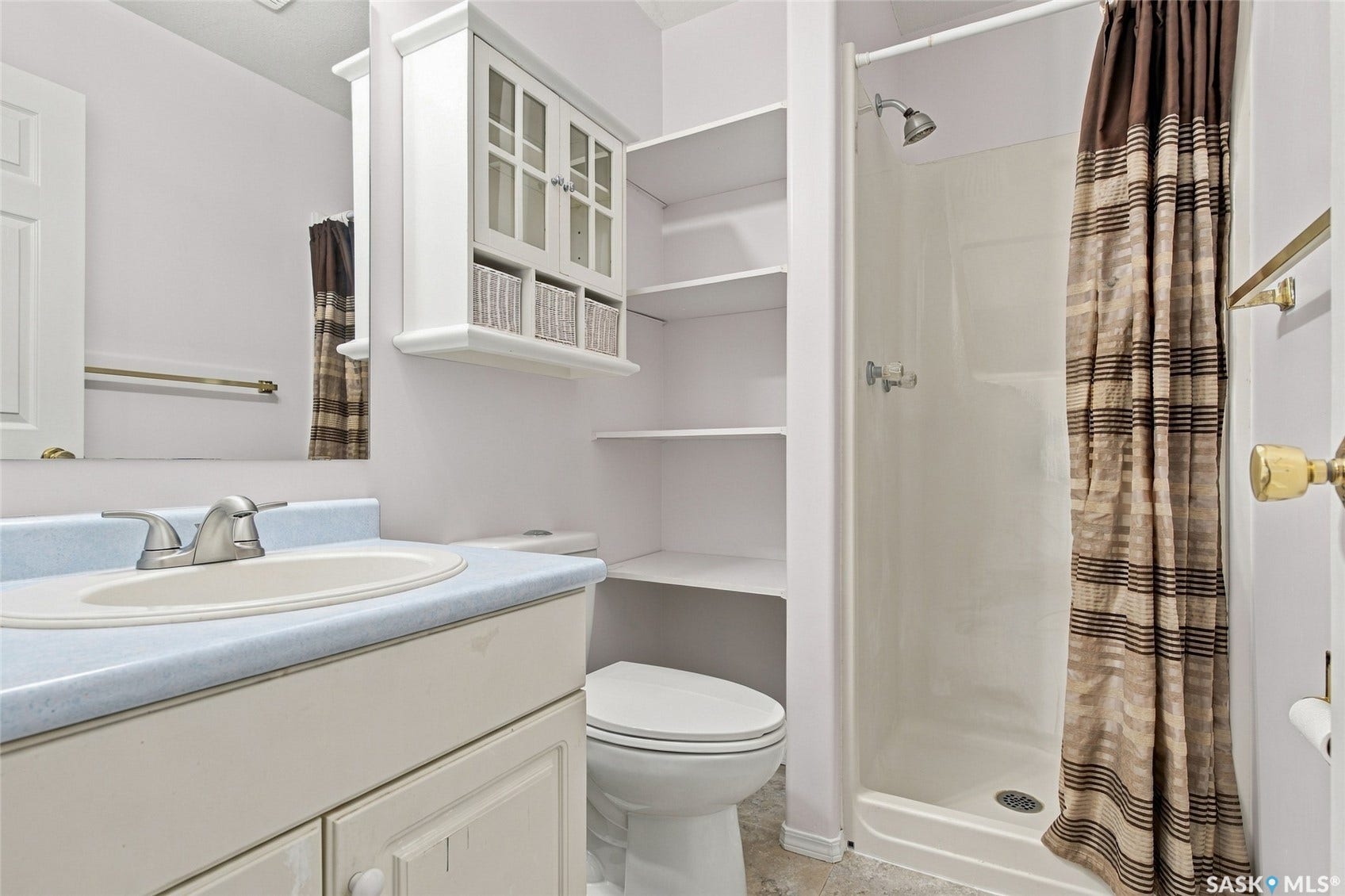 Bathroom featuring a single vanity, a shower stall, integrated shelving, and a wall-mounted cabinet