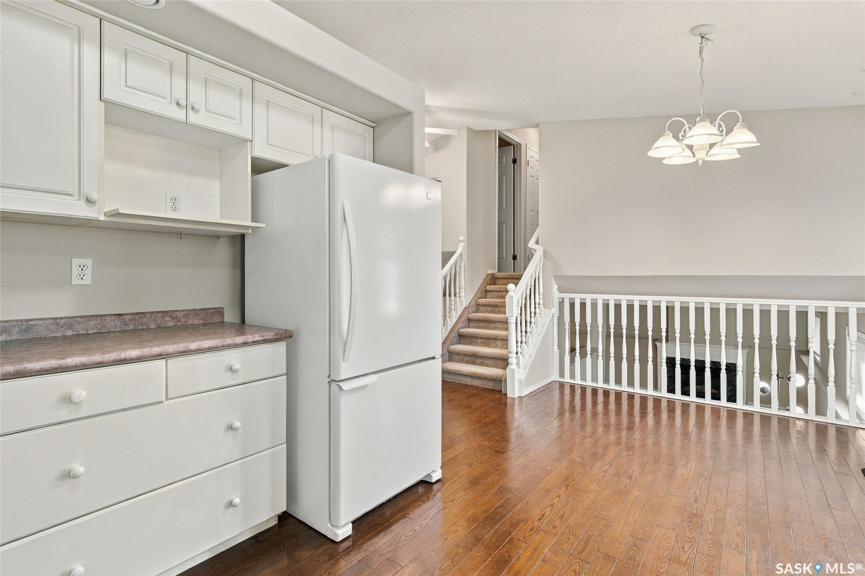 Wood-finish flooring throughout, white cabinetry with upper and lower storage, white railing with balusters, and a multi-arm chandelier