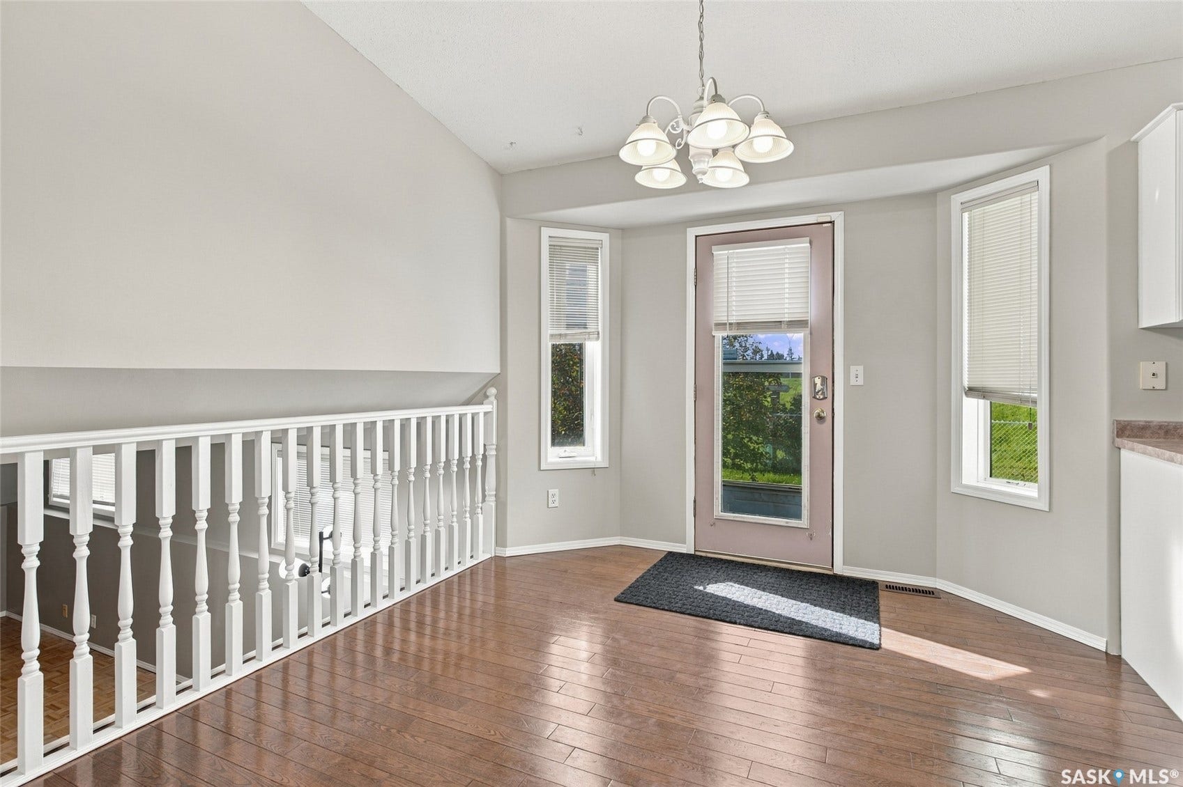 Bright foyer featuring hardwood flooring, white wainscoting, and a curved staircase with turned balusters