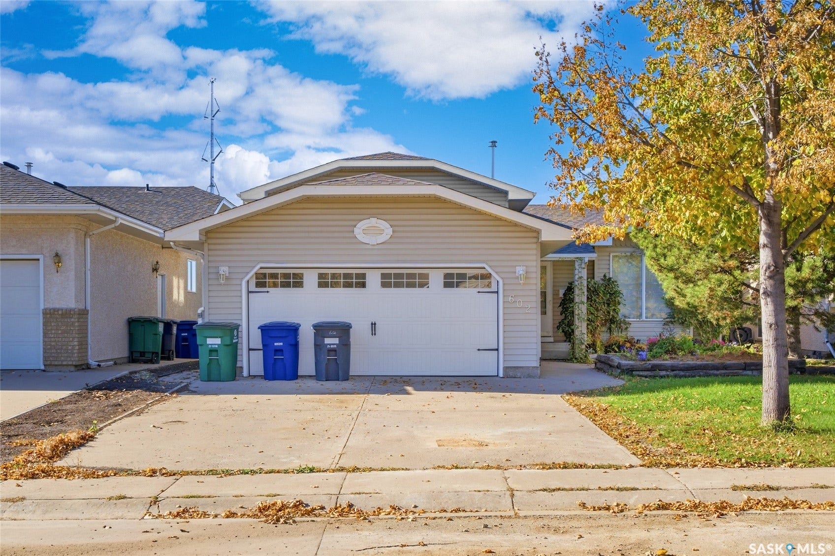 Attached two-car garage, concrete driveway, and front yard with mature landscaping