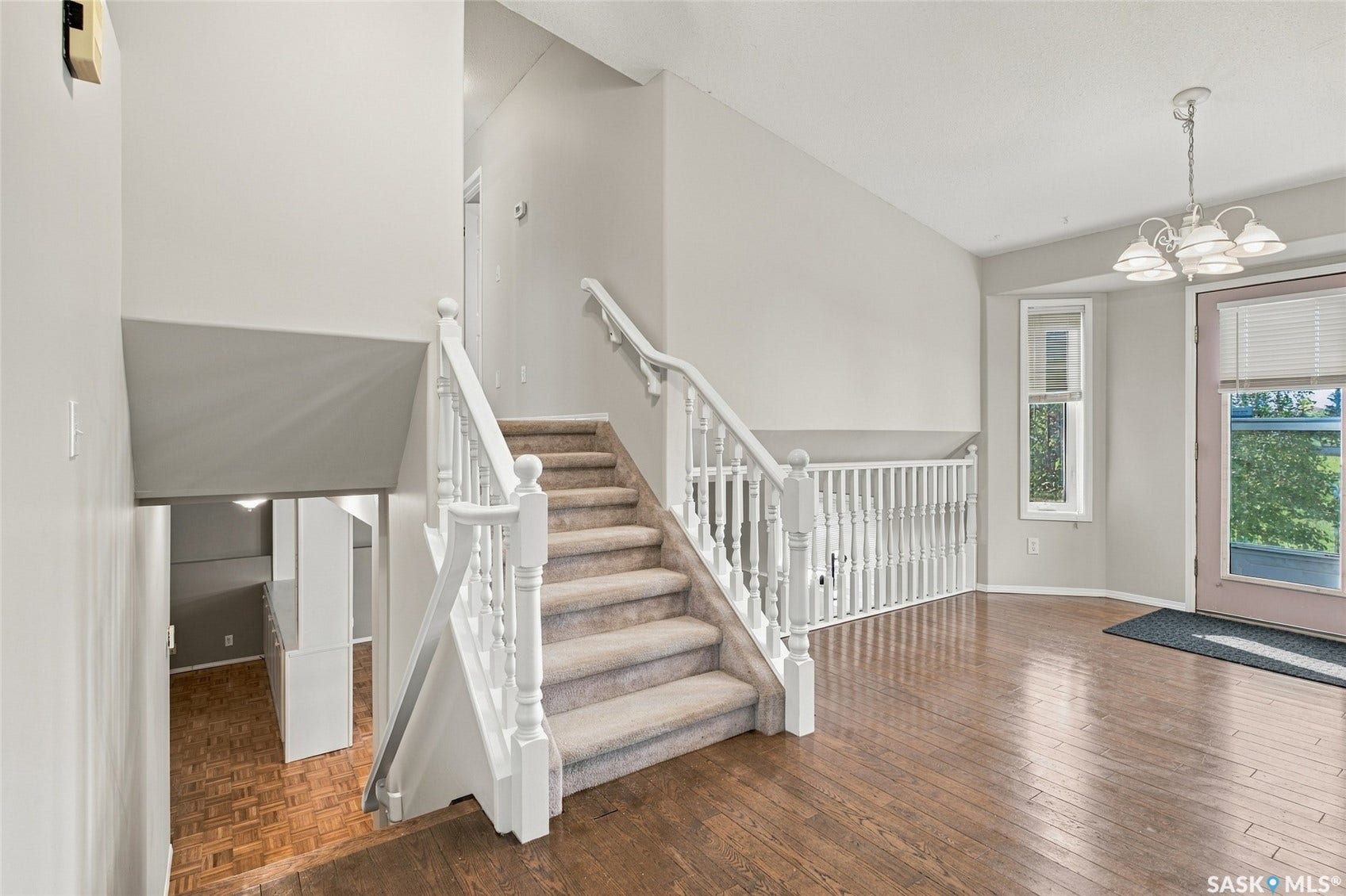 Hardwood flooring, carpeted staircase, white banister, bay window, and a white chandelier