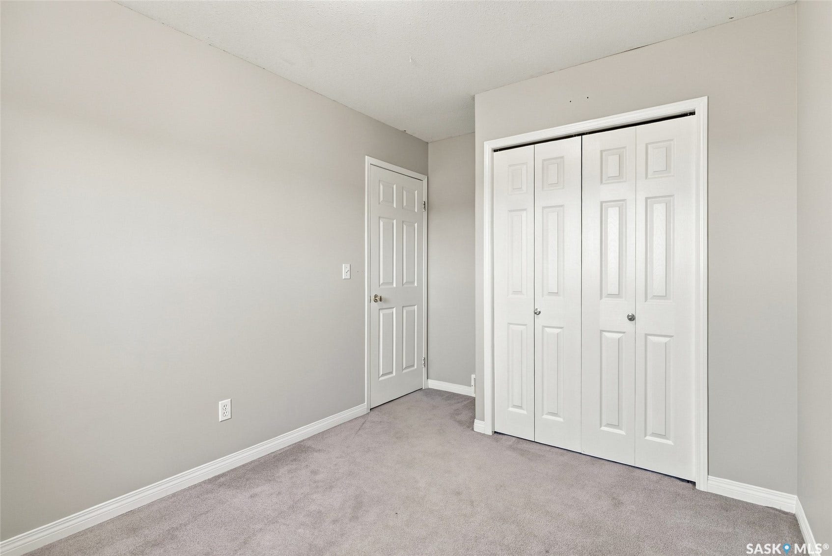 Gray carpet flooring with white trim, a white paneled door, and a white bi-fold closet door