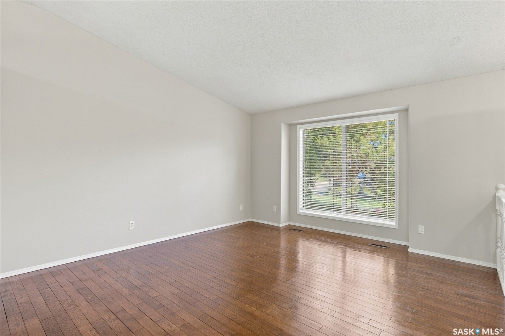 Spacious room featuring wood-finish flooring, a large window with blinds, and light-toned walls