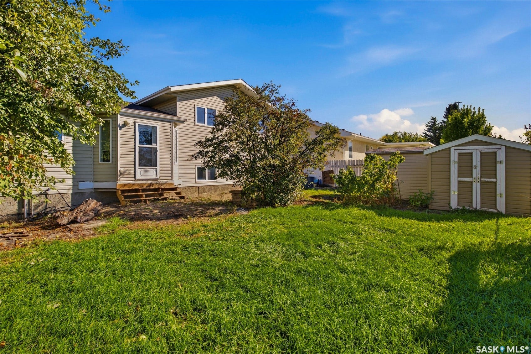 Expansive lawn area featuring a utility shed with dual doors, a rear entrance with wooden steps, and mature trees