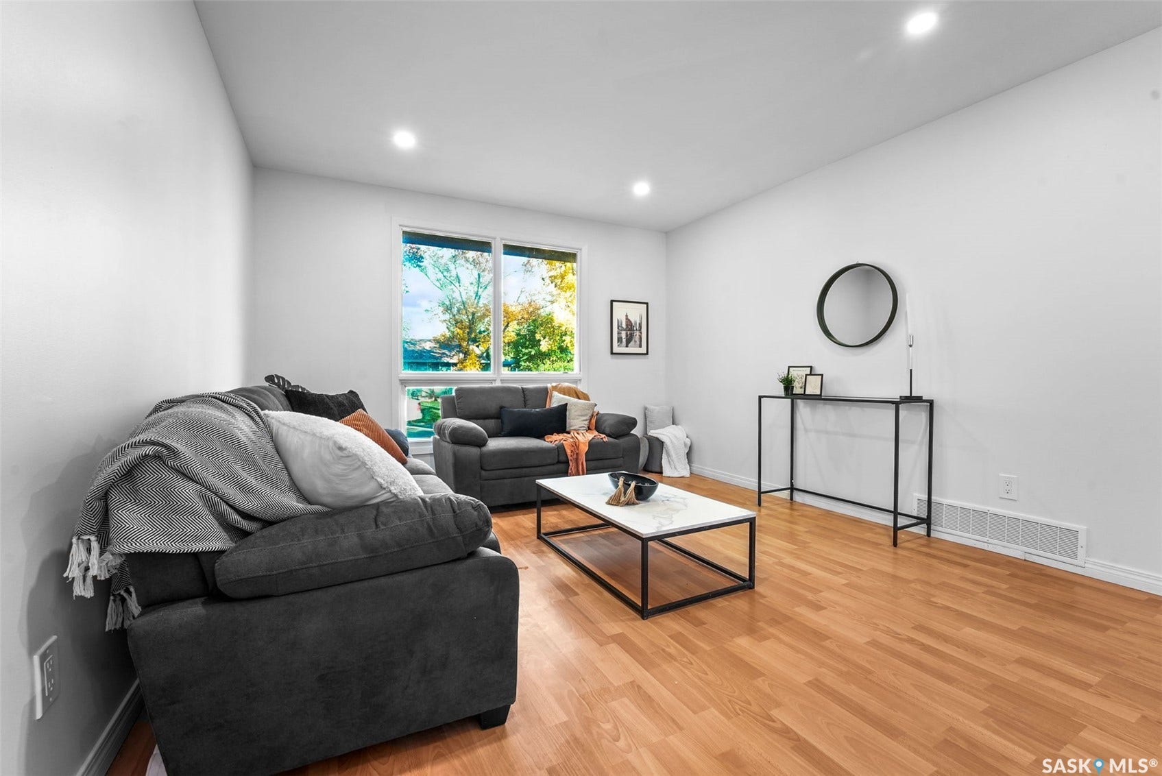 Bright, open living space featuring warm wood-finish flooring, recessed ceiling lighting, and large windows with natural light