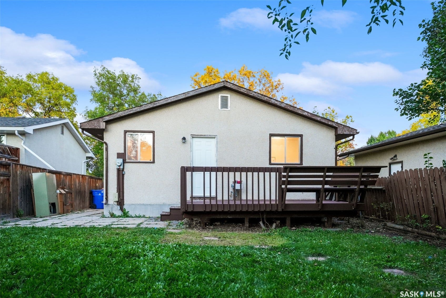 Rear exterior featuring a wood deck, stucco siding, and a fenced yard with a grass area