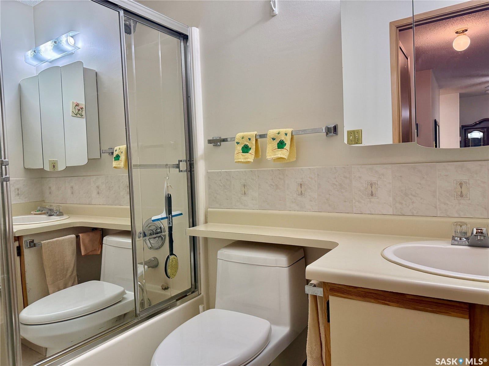 Ceramic tile backsplash, built-in medicine cabinet, integrated sink, and white bathtub with glass enclosure