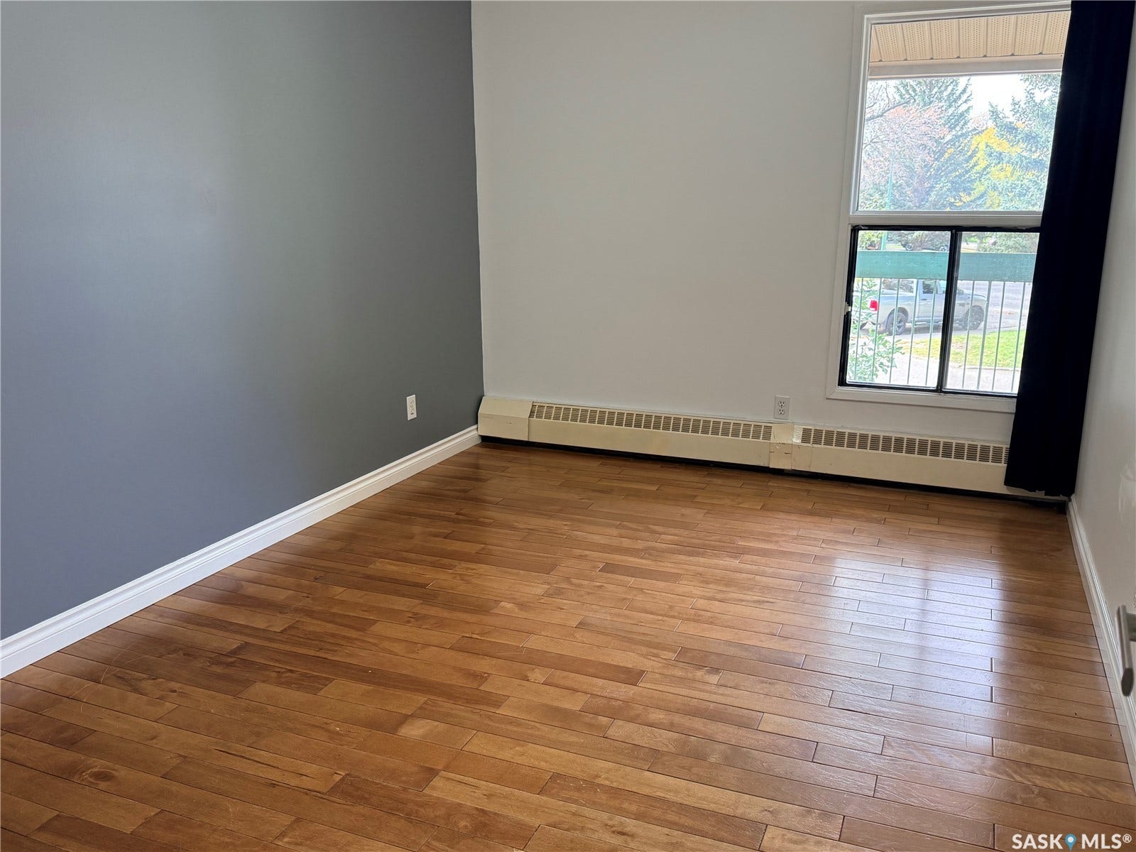 Wood-finish flooring with white baseboards, a neutral color palette featuring a gray accent wall, and a large window