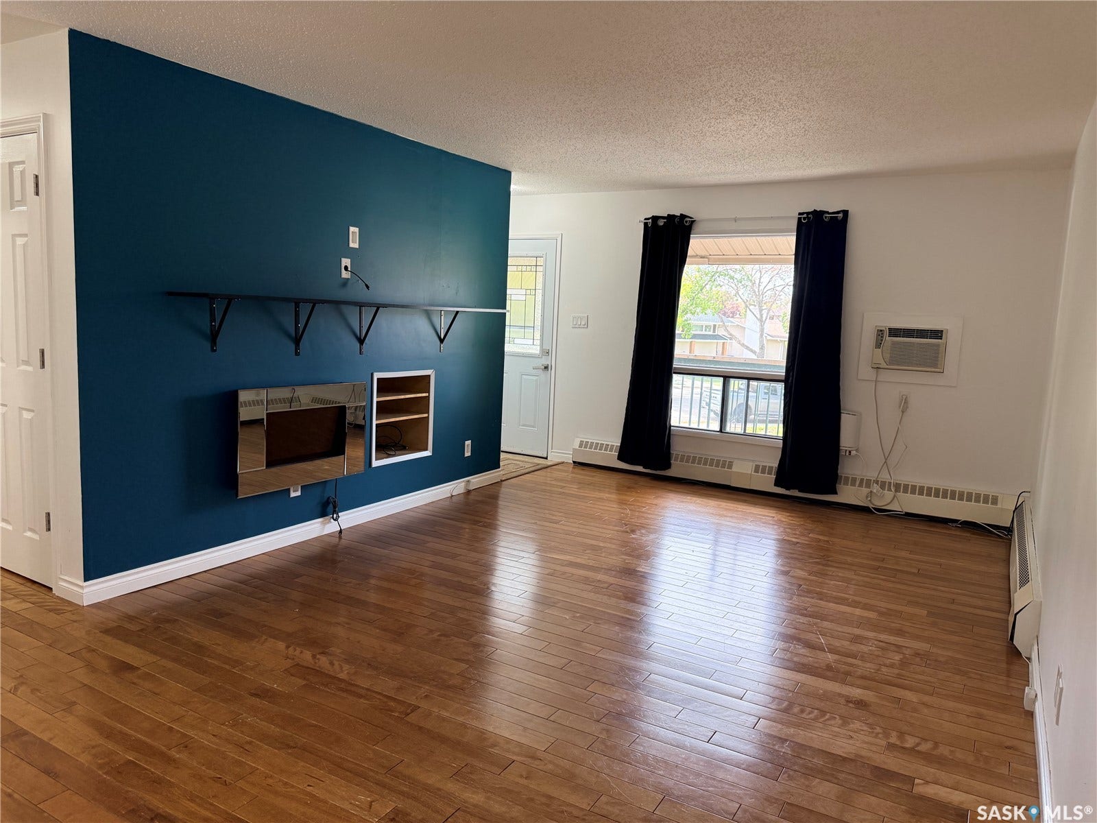 Hardwood-finish flooring, accent wall, built-in shelving, window with natural light, and wall-mounted air conditioning unit