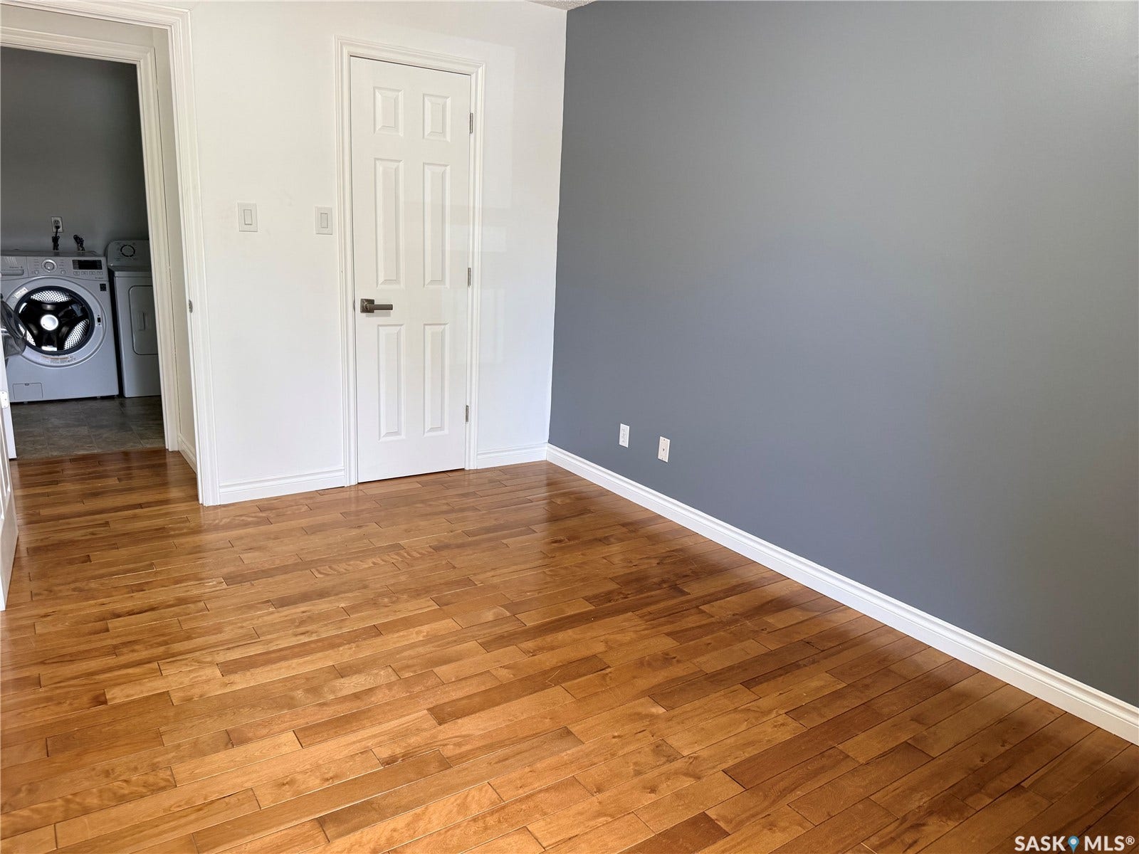 Hardwood flooring, painted walls, white trim, and a paneled door with a lever handle