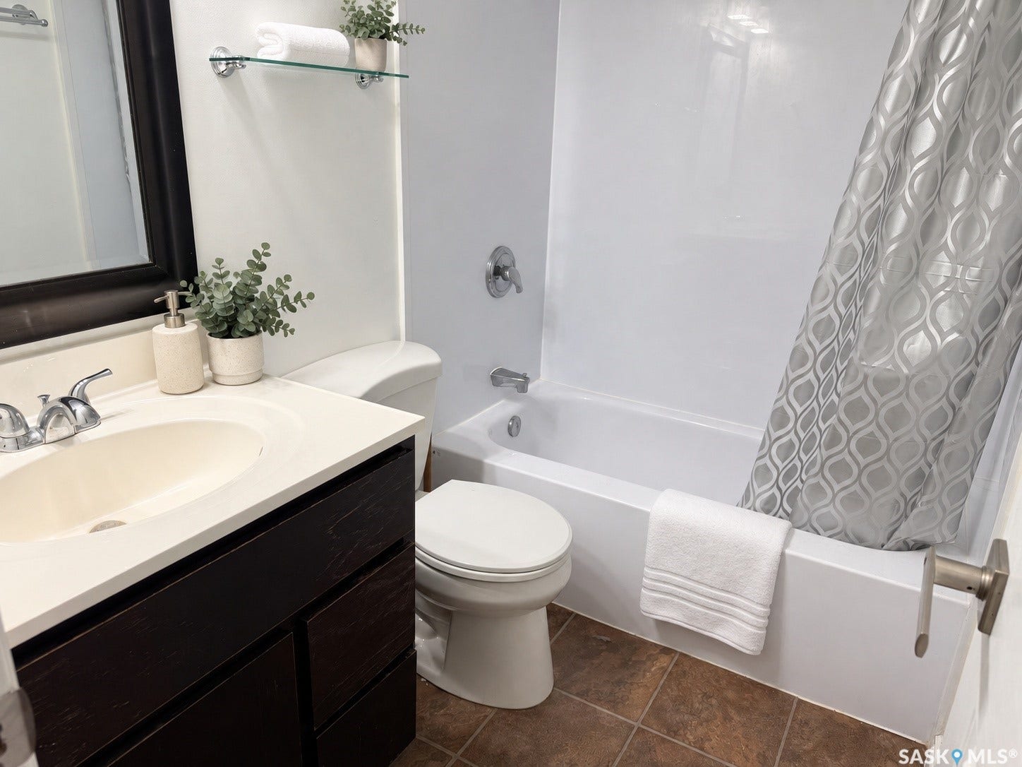 Bathroom featuring a dark wood-finish vanity with a light-colored countertop, an integrated sink, a built-in bathtub, and a glass wall shelf