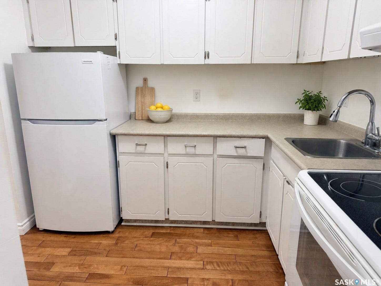 Kitchen featuring wood-finish flooring, white cabinetry, laminate countertops, and a stainless steel sink with a chrome faucet