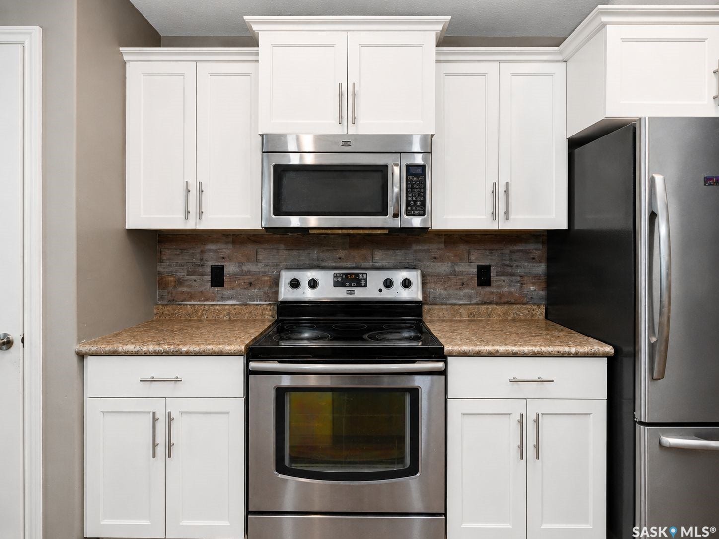 White shaker-style cabinetry with crown molding, stainless steel appliances, a textured backsplash, and speckled countertops