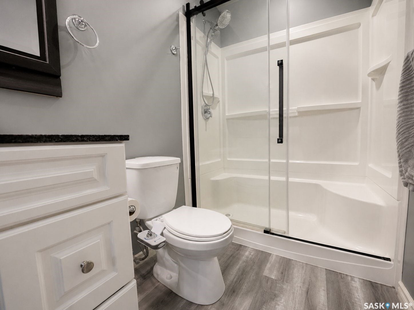 White vanity with a dark countertop, walk-in shower with a sliding glass door, and wood-finish flooring