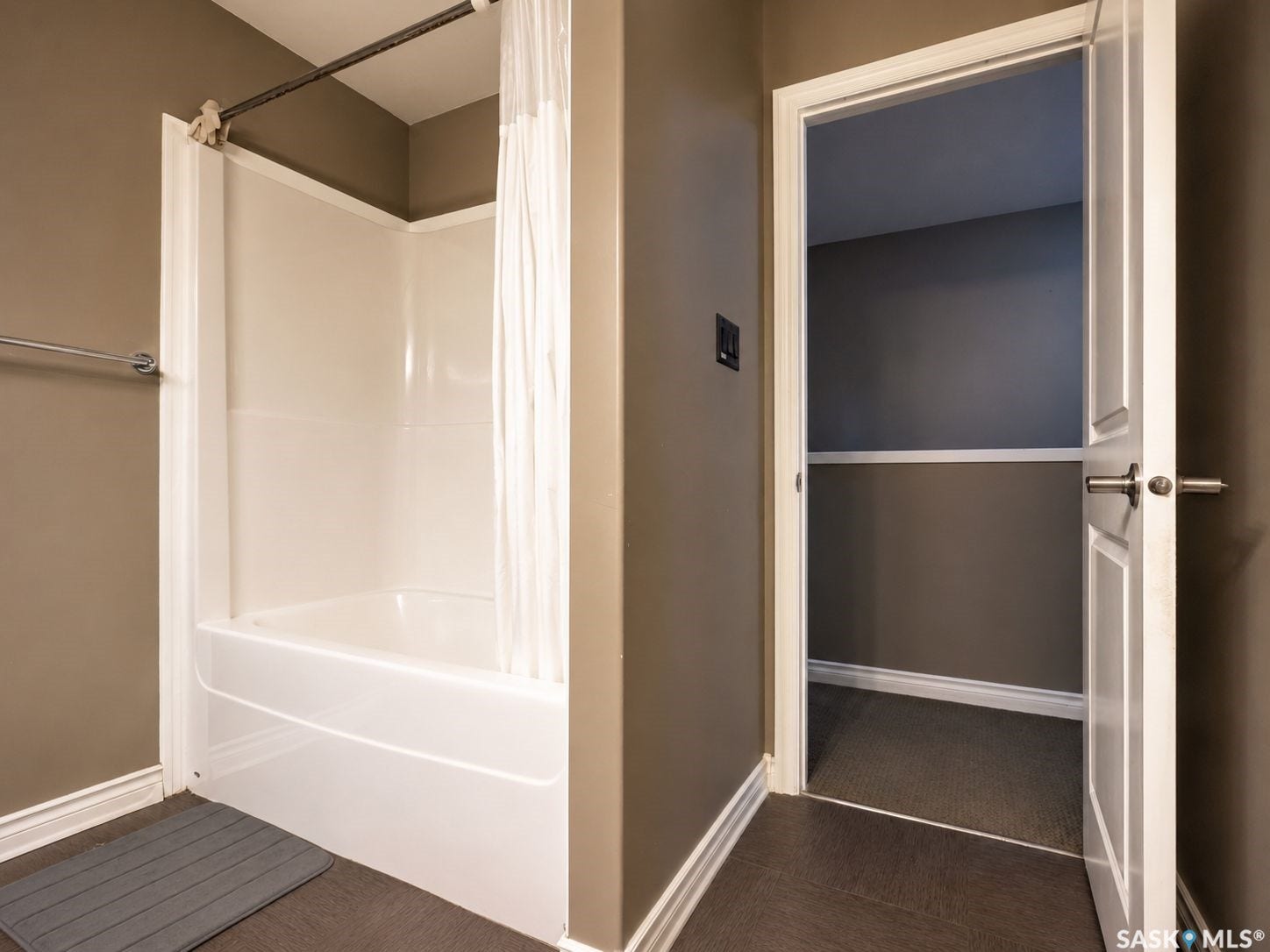 White bathtub with an integrated shower, chrome towel bar, and a white interior door with paneling