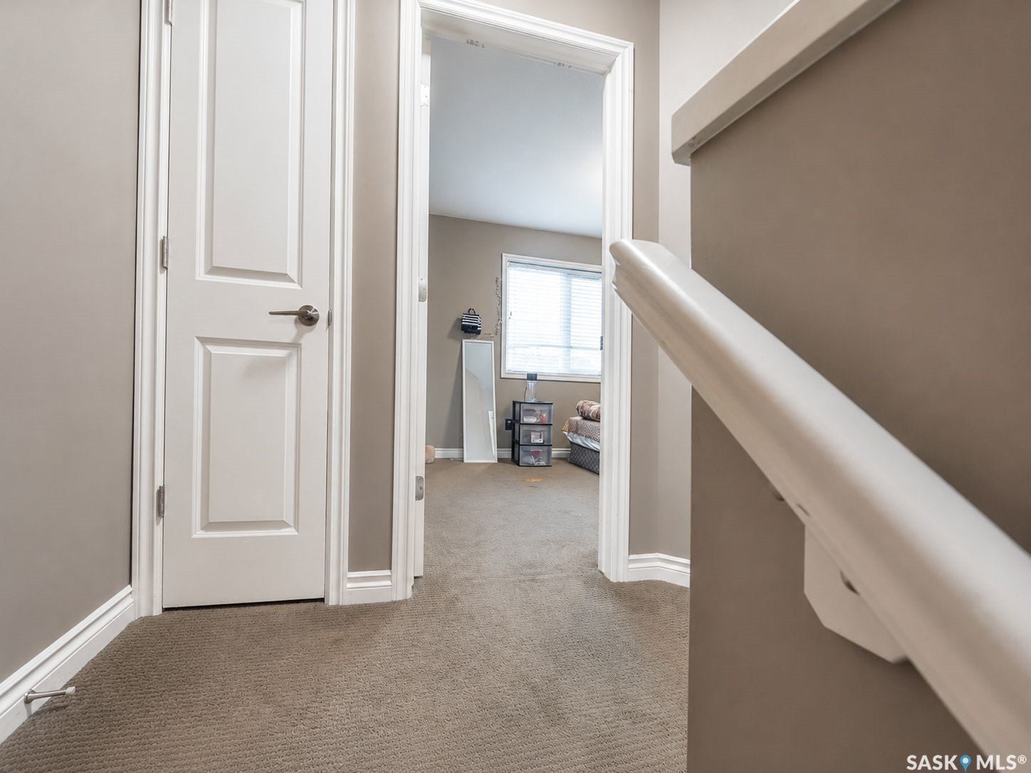 Carpeted hallway featuring a white handrail, white trim, and a paneled interior door