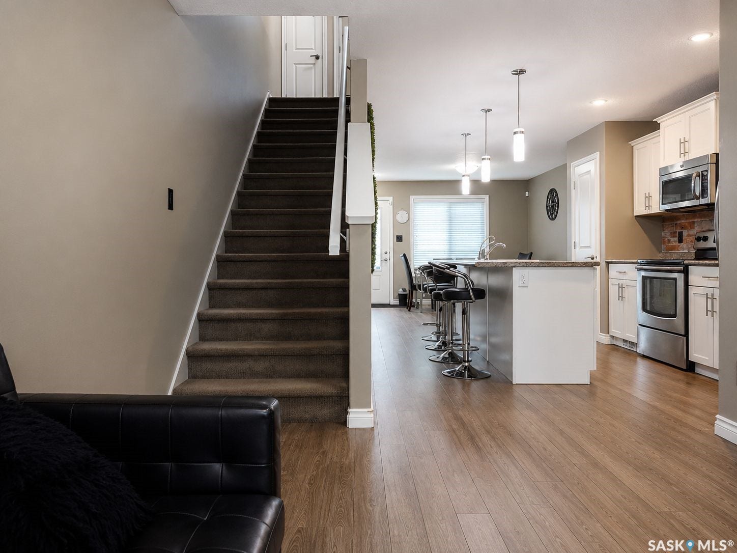Wood-finish flooring, white kitchen cabinetry, stainless steel appliances, kitchen island with seating, and pendant lighting