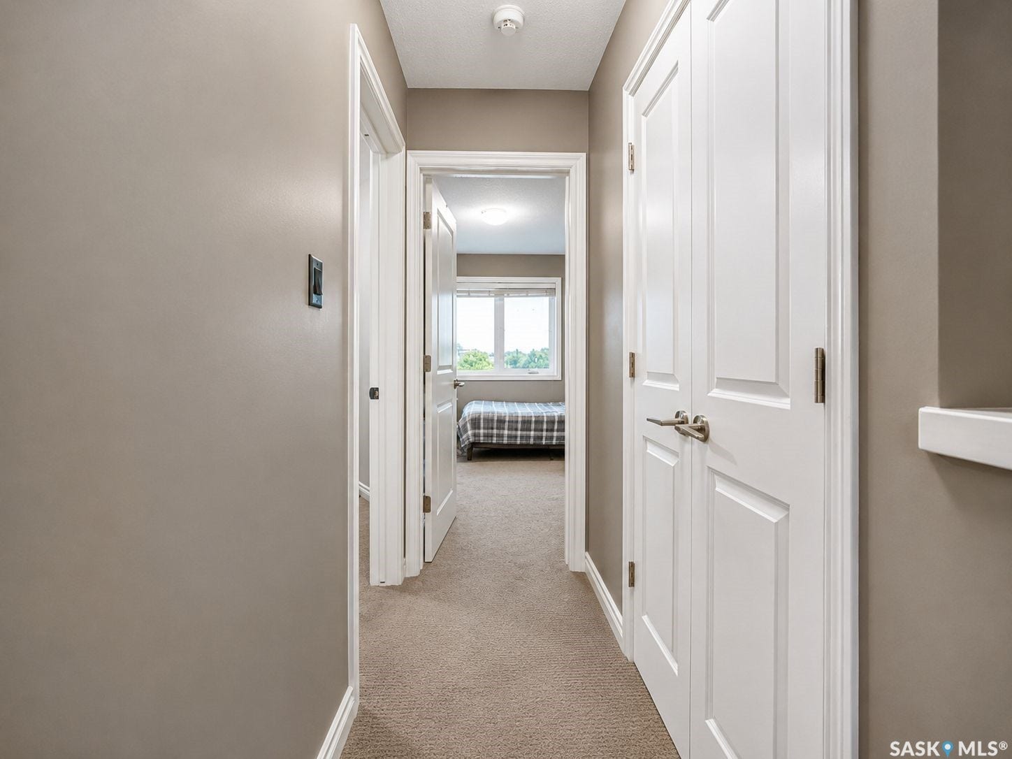 Carpeted hallway with neutral wall tones, white trim, and panel doors