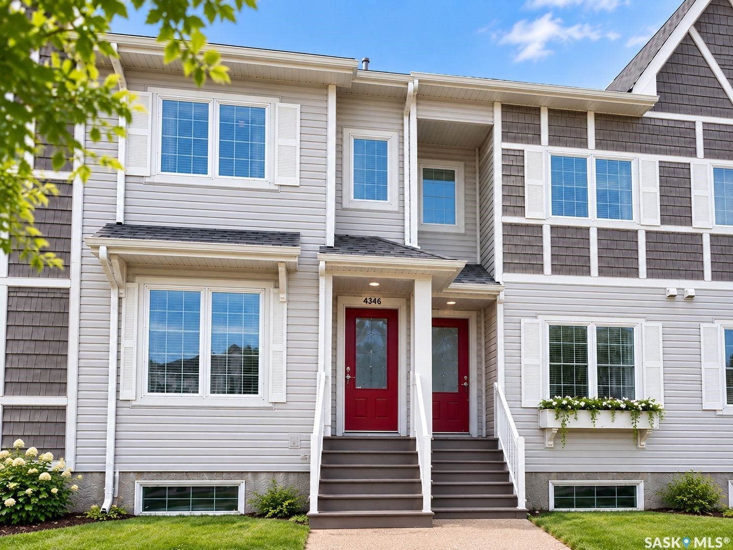 Light grey siding with shake accents, red entry doors, white window shutters, window boxes, and a low-maintenance lawn