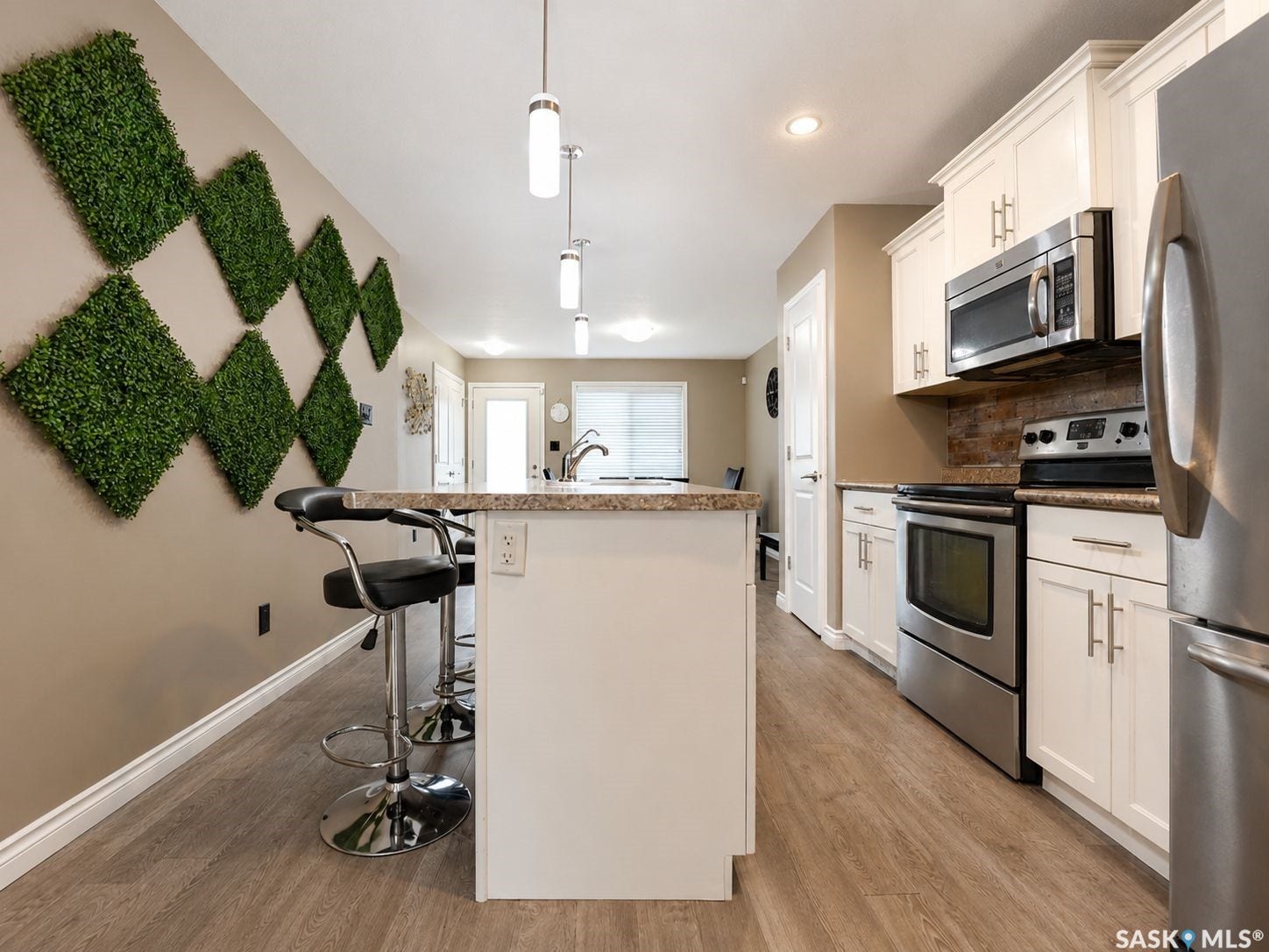 Modern kitchen featuring light cabinetry, stainless steel appliances, a center island with countertop seating, wood-finish flooring, and pendant lighting