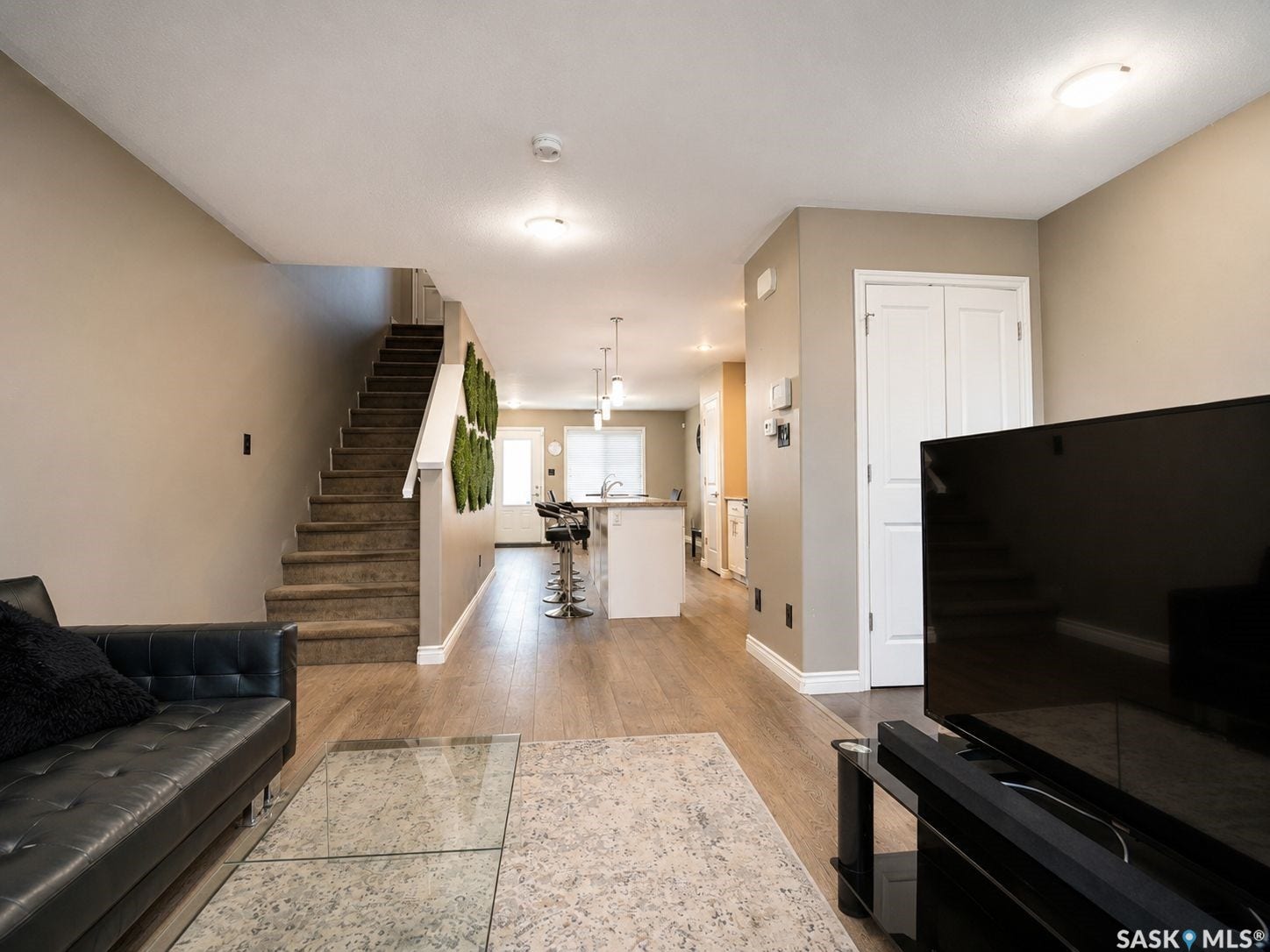 Wood-finish flooring, staircase with carpeted treads, white built-in bi-fold doors, white baseboards, and ceiling-mounted lighting fixtures
